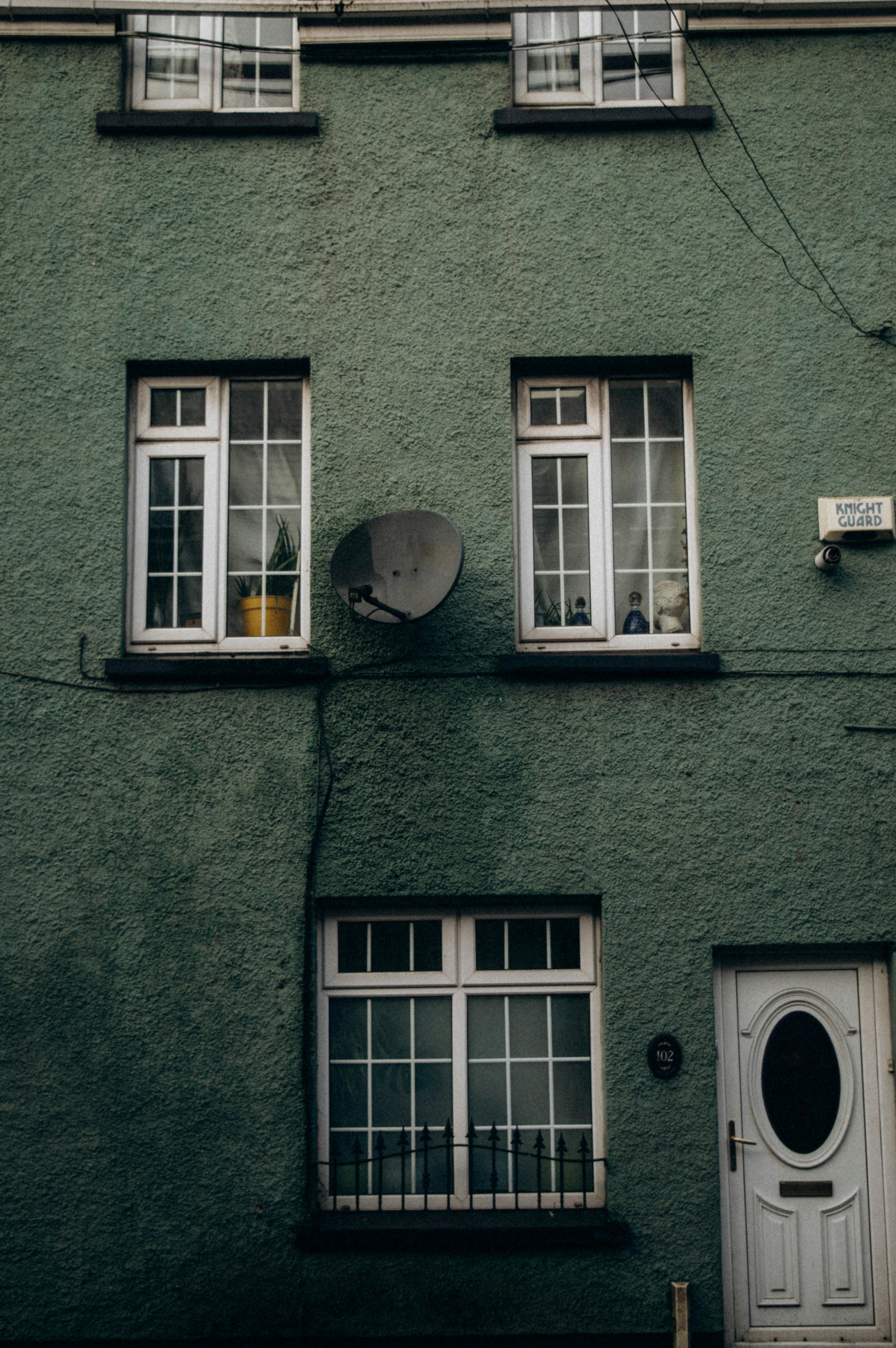 Green exterior wall of a residential building featuring windows and a satellite dish, capturing urban architecture.