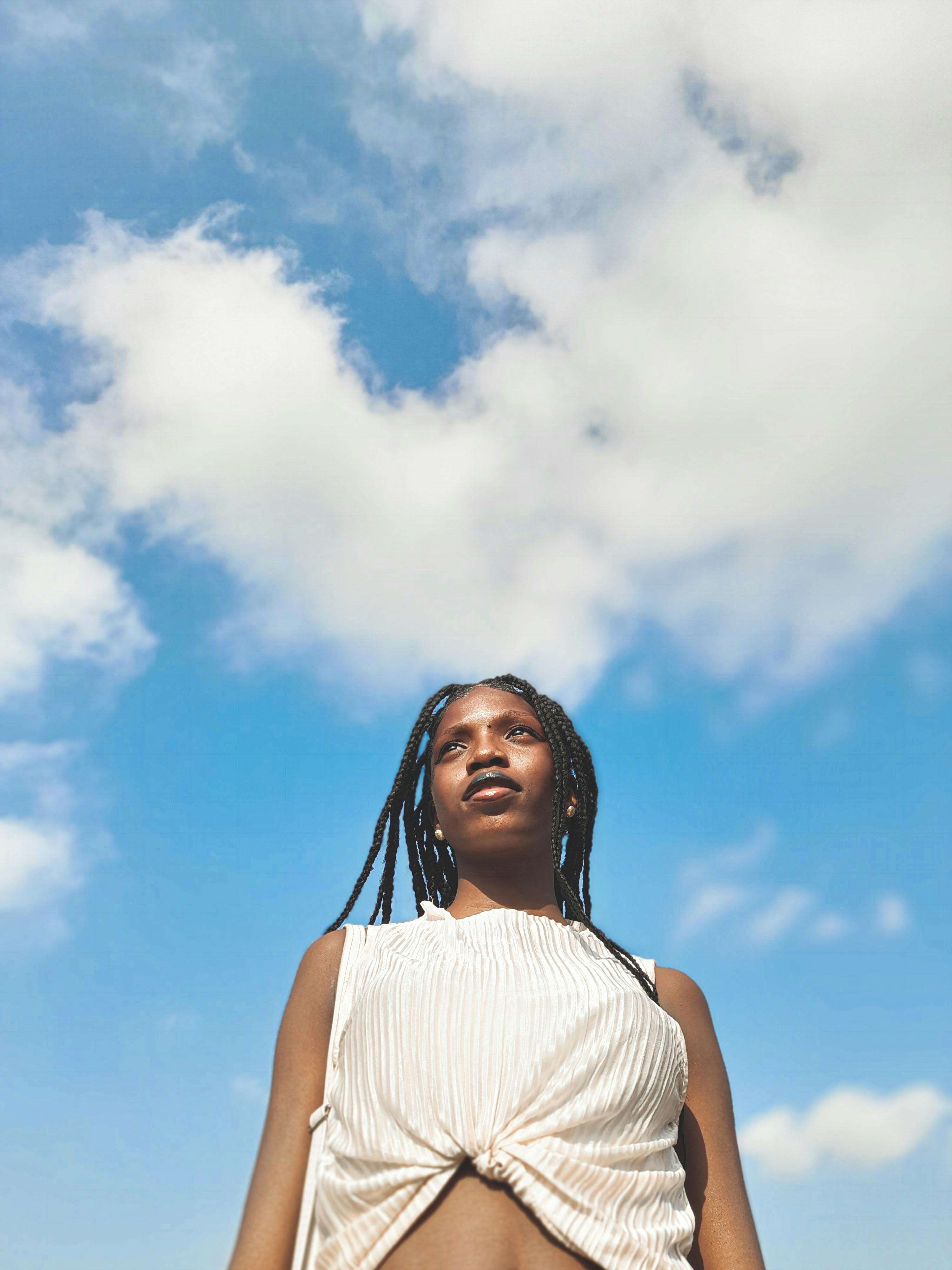 Portrait of a woman in Lagos with afro braids looking upwards against a blue sky.