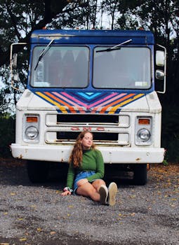 一名年轻女子坐在户外一辆涂有彩色油漆的老式白色卡车前