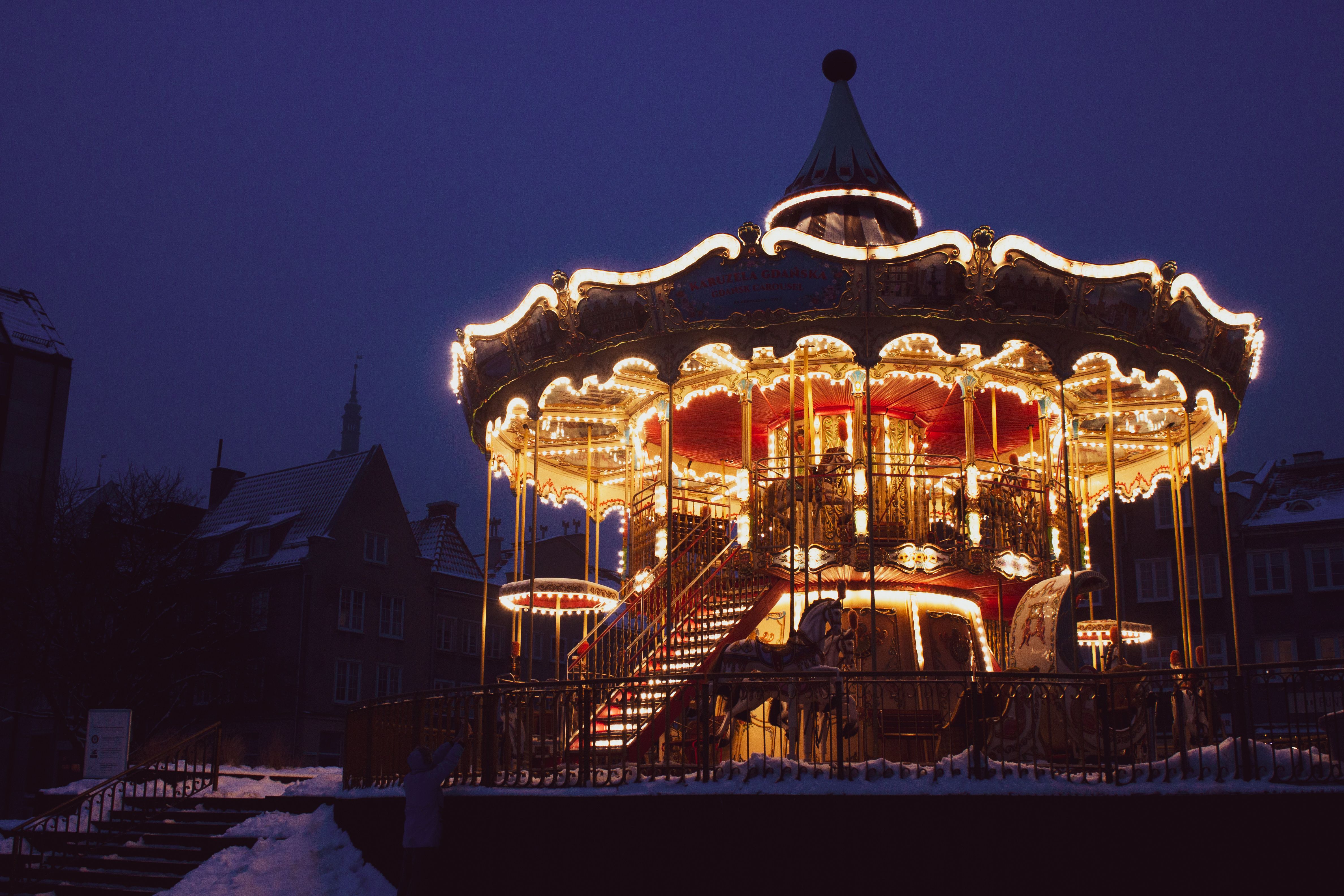 A vintage carousel beautifully illuminated at night in a snowy Gdańsk cityscape, creating a magical urban scene.
