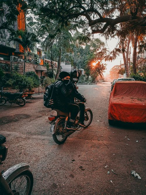 Free Two motorcyclists riding through a tree-lined urban street during sunset. Stock Photo