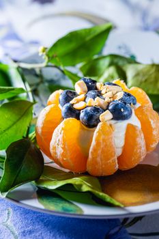 Tangerine topped with blueberries and nuts on a leafy plate, ideal for healthy snacking.