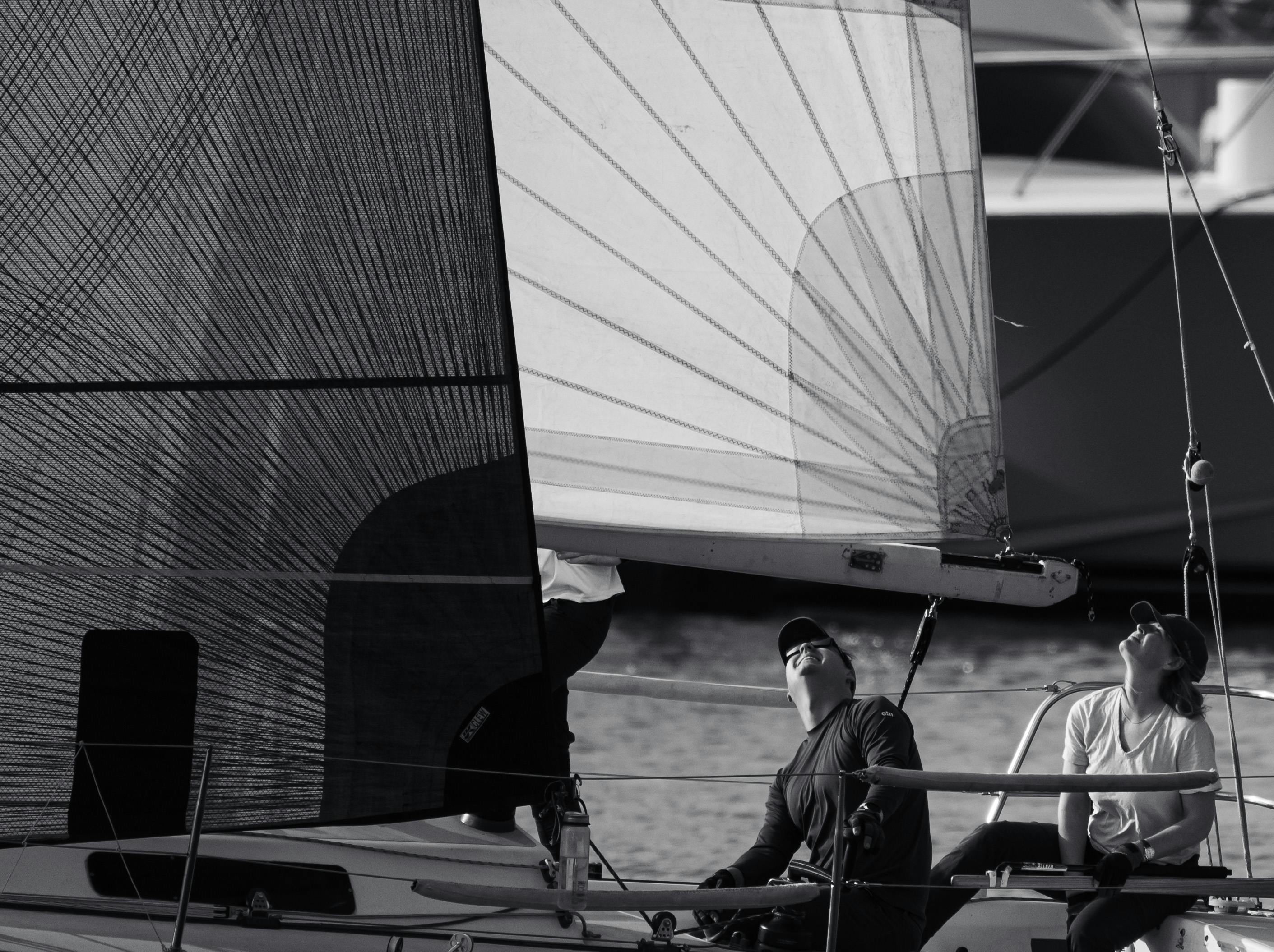 Black and white close-up of a sailboat with two adults navigating under the sails.