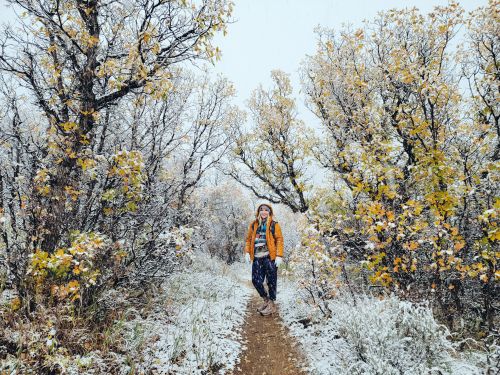 Free Woman exploring a snowy forest trail during early winter transition, amidst vibrant autumn leaves. Stock Photo