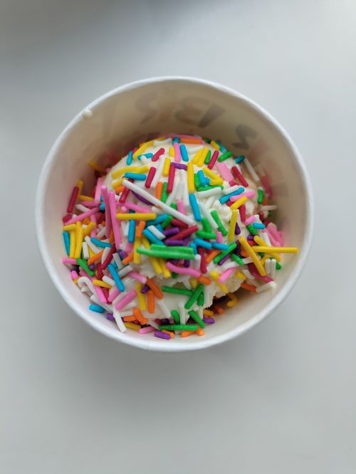 Free A vibrant scoop of ice cream decorated with colorful sprinkles in a white paper cup. Stock Photo