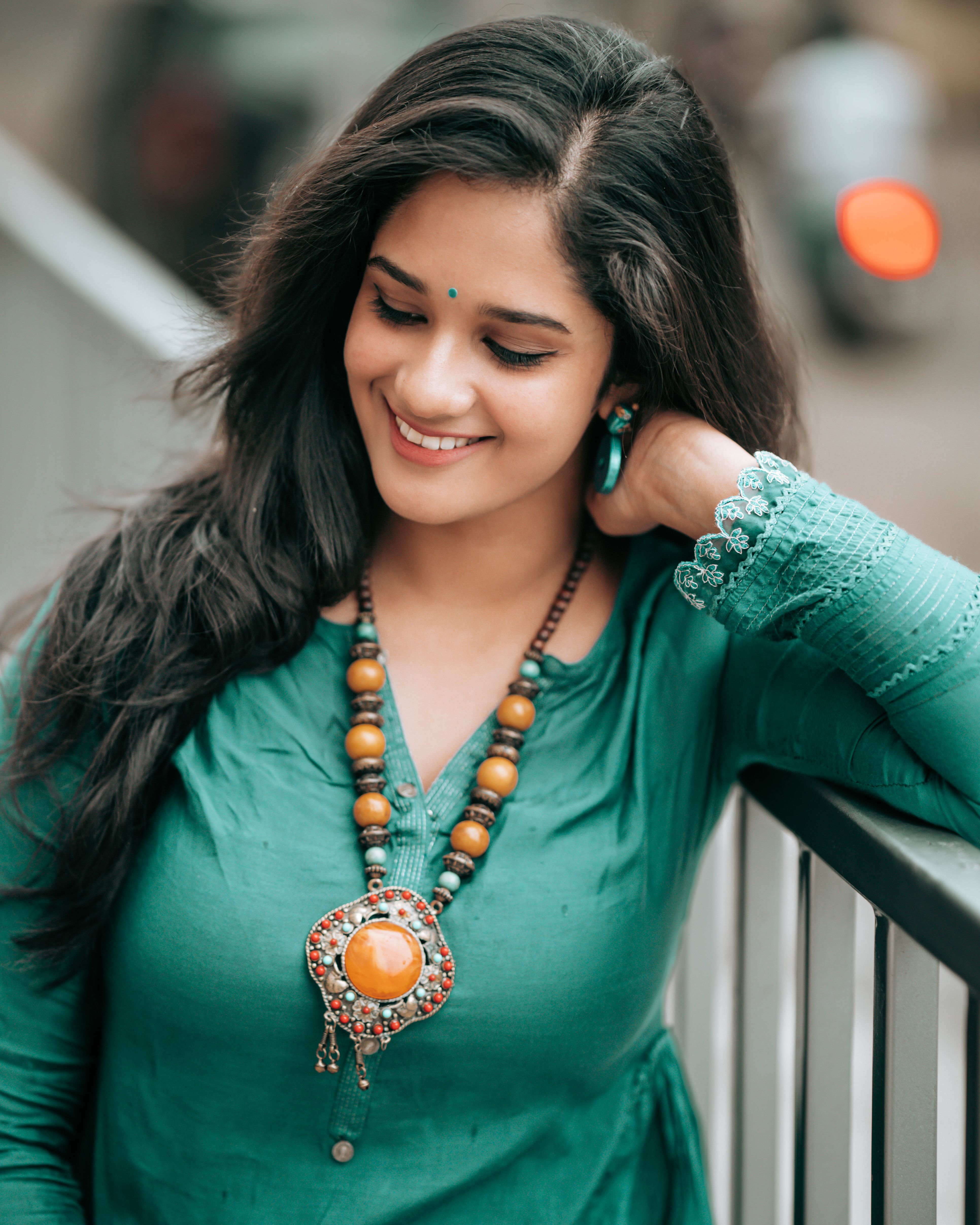 Portrait of a smiling South Asian woman with bindi and necklace in green dress, enjoying a serene moment outdoors.