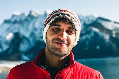 Free Smiling man in a red jacket and beanie with a snowy mountain background in Banff. Stock Photo