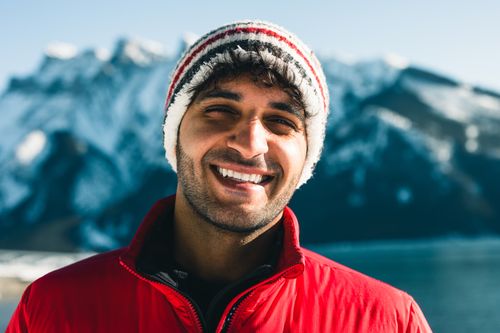 Free Smiling man wearing a beanie and red jacket with icy mountains in the background, Banff, Canada. Stock Photo