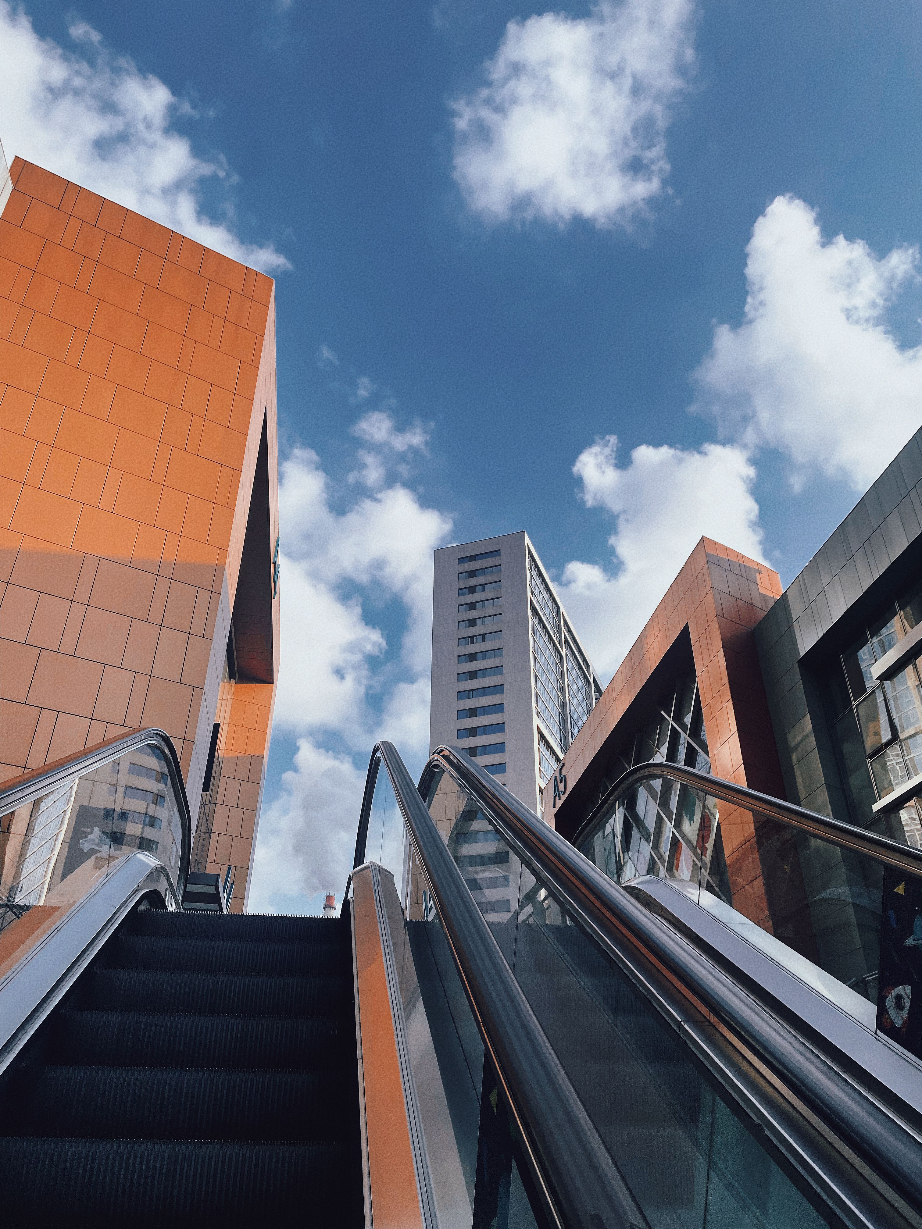 Vertical shot of modern buildings and escalator against a blue sky with clouds in Dalian, China.