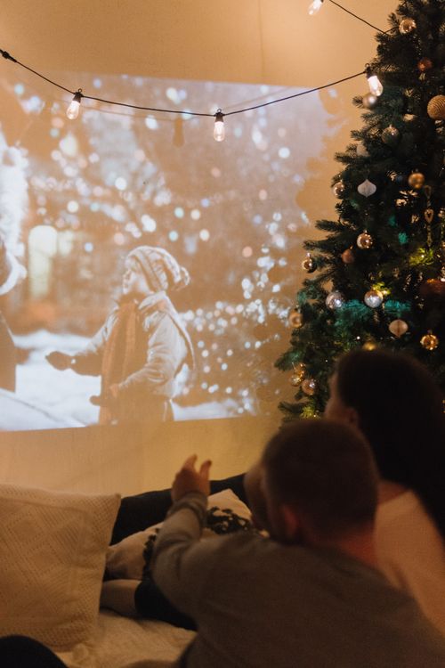 Free Couple enjoying a festive movie night with a Christmas tree and projector indoors. Stock Photo