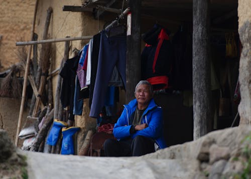 Elderly Man Sitting in front of a House with Laundry Drying on a Line above Him 