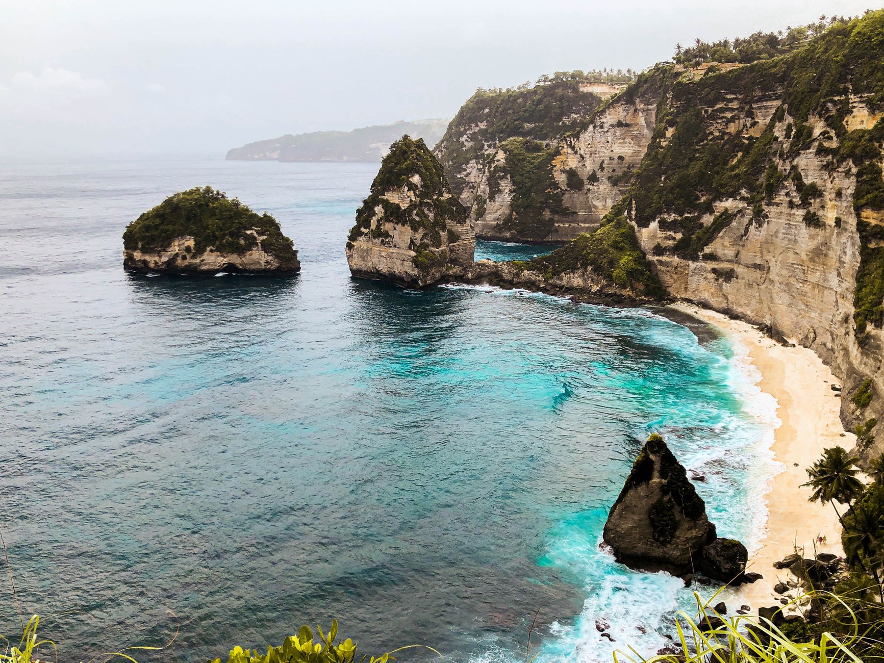 Stunning aerial view of Kelingking Beach, Bali, with turquoise waters and lush cliffs.