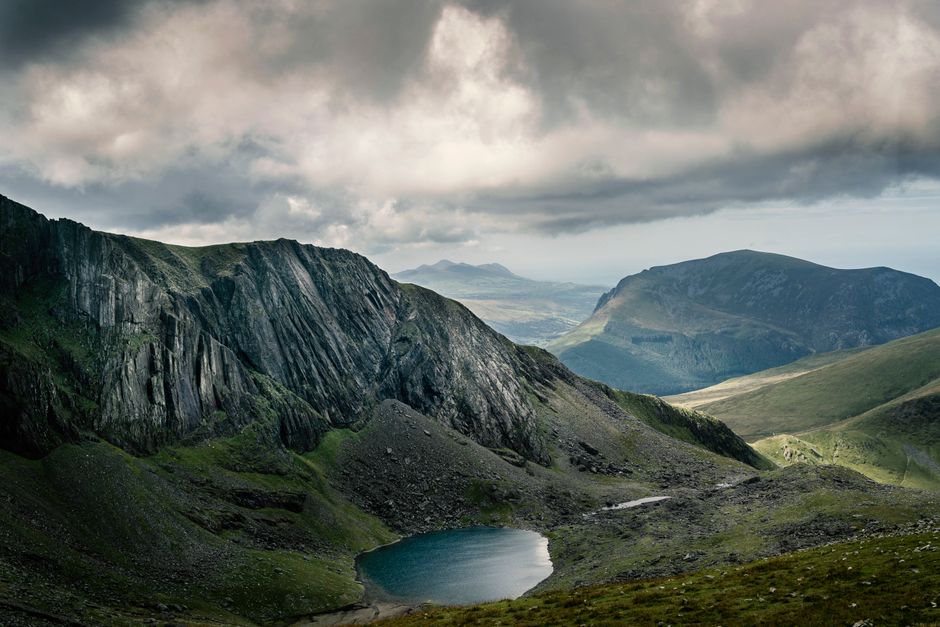 Breathtaking view of rocky mountains and serene lake under a dramatic cloudy sky.
