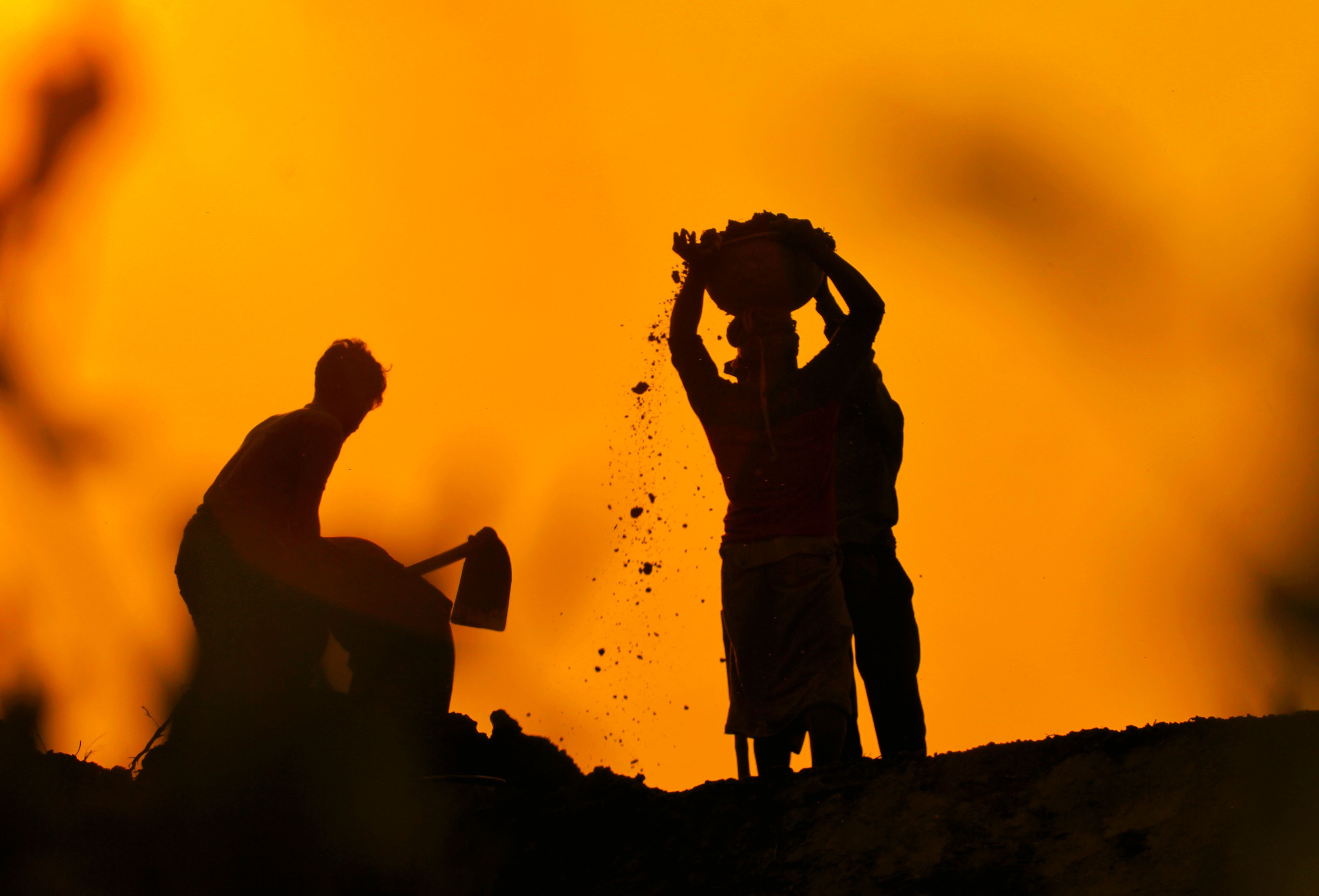 Silhouette of workers standing and handling soil during sunset, showcasing rural life.