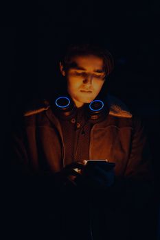 Portrait of a young man with headphones using a smartphone in a dimly lit setting.