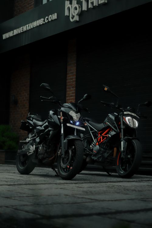 Free Dark-themed photo of two parked motorcycles on a sidewalk in an urban setting. Stock Photo