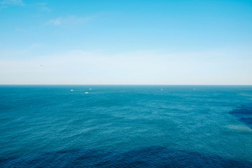 Free A serene aerial seascape with boats on a clear horizon under a bright blue sky. Stock Photo
