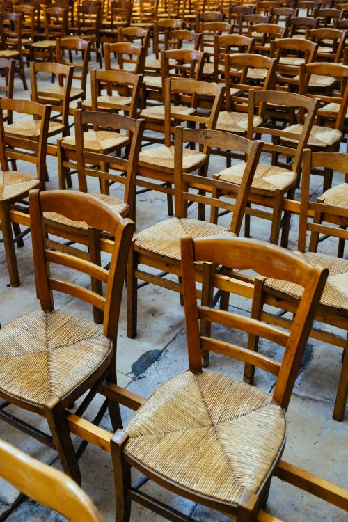 Free Vertical shot of numerous wooden chairs lined up indoors, creating a patterned texture. Stock Photo