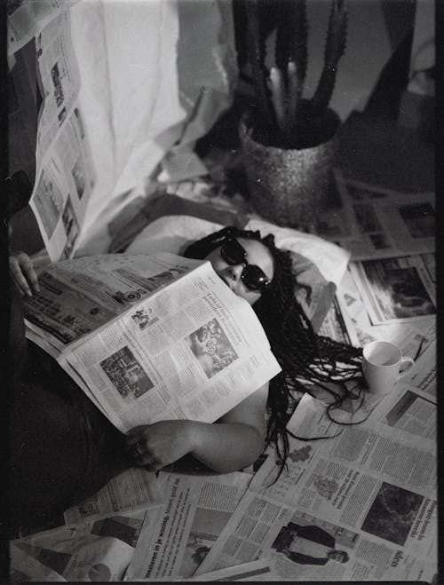 A Grayscale of a Woman Lying Down on Newspapers