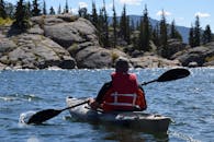 在清澈的蓝天下，划独木舟于高山湖泊，四周环绕着岩石和树木