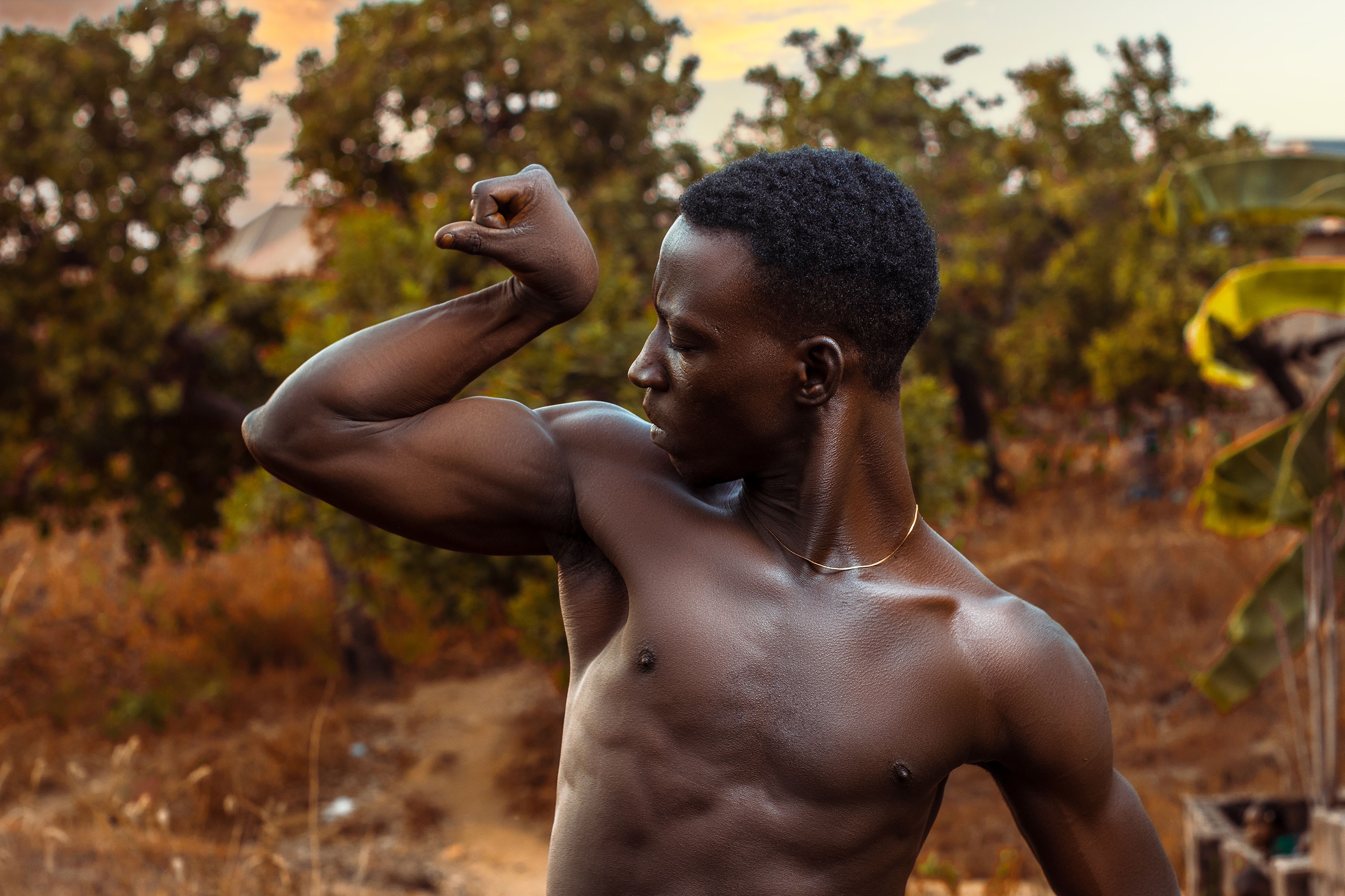 Shirtless African man showcasing muscles in a sunny outdoor setting in Nigeria.