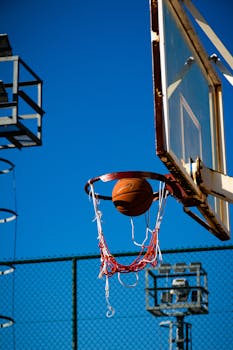A basketball midair inside hoop against a clear blue sky in an outdoor court.
