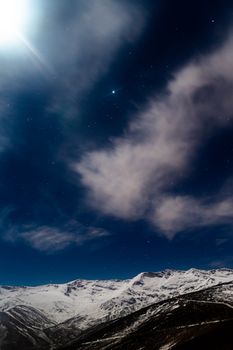 Starry night sky with clouds and snowy peaks at Uludağ, Turkey, captured in a long exposure shot.