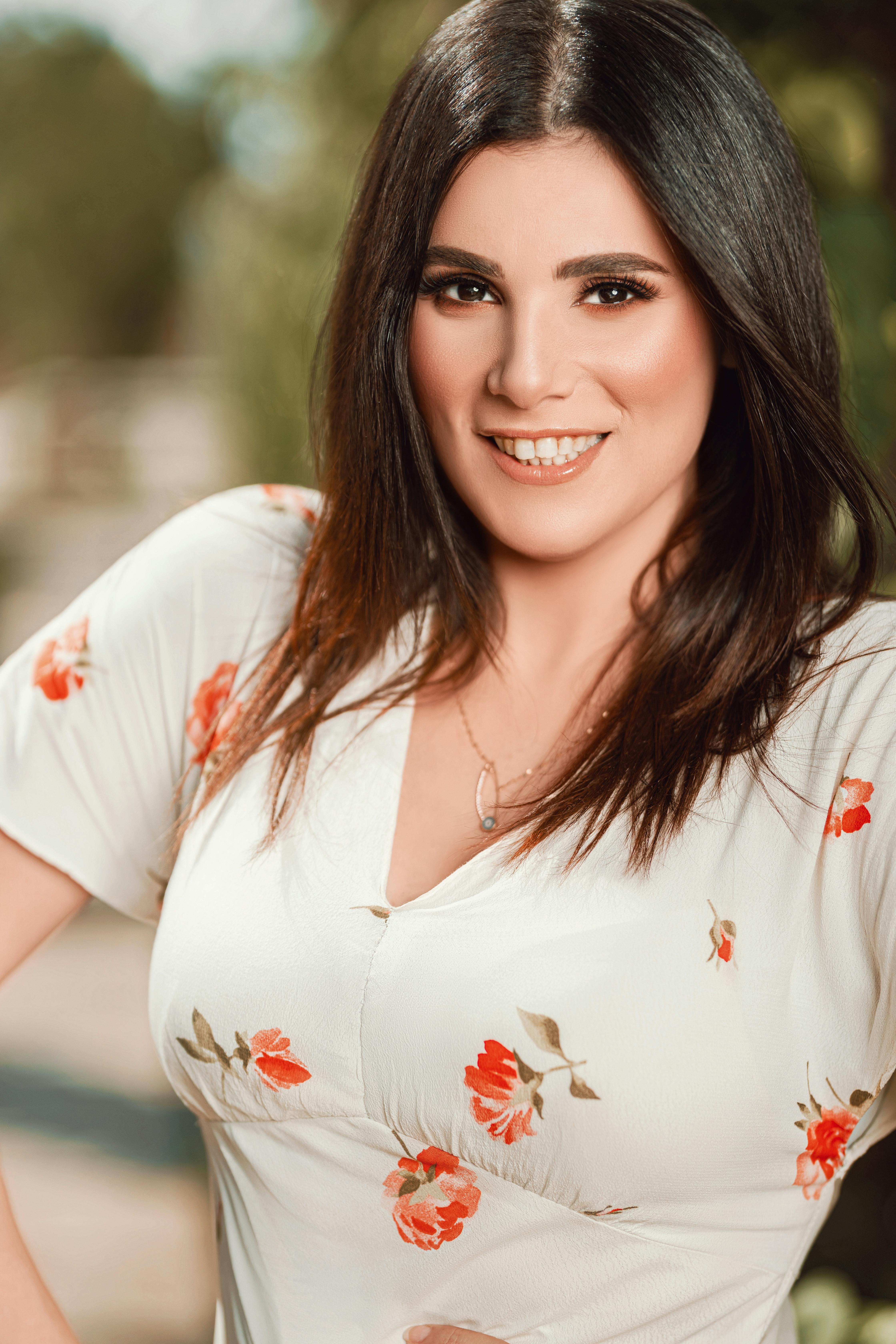 Portrait of a smiling woman wearing a floral dress, enjoying a sunny day outside.