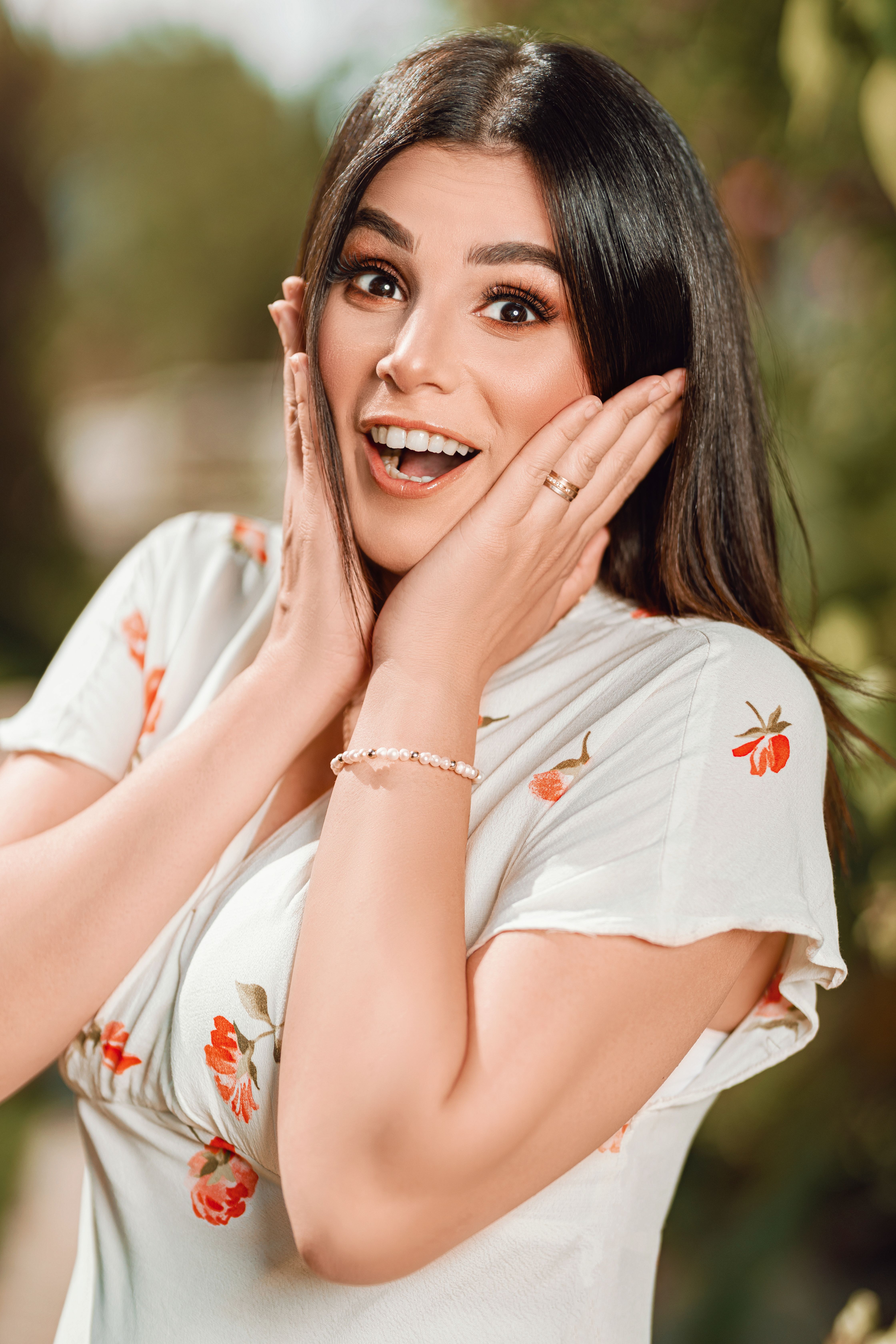 Delighted woman with hands on face showing surprise in a sunny garden.