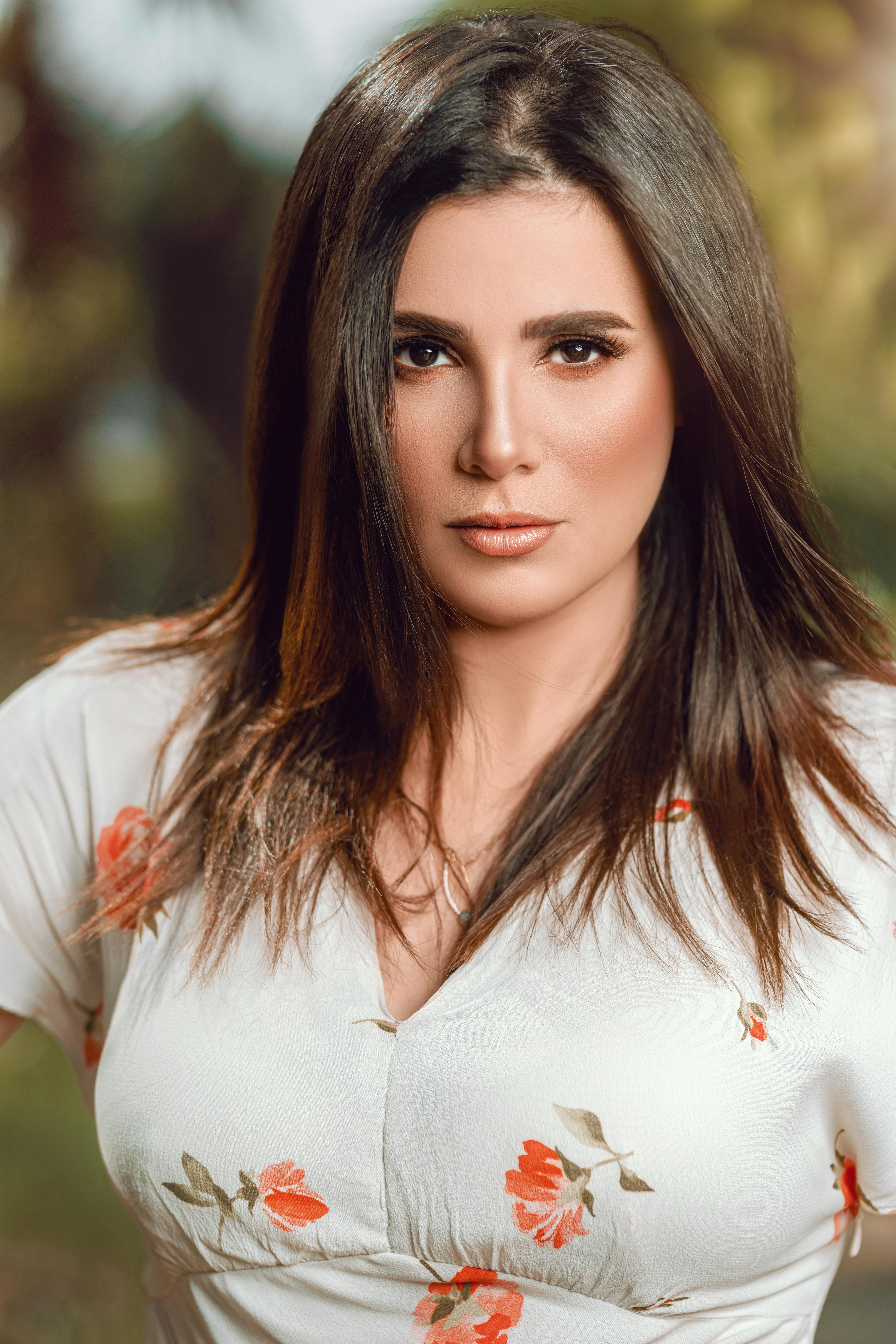 A woman poses outdoors in a floral dress with a soft, sunny background.