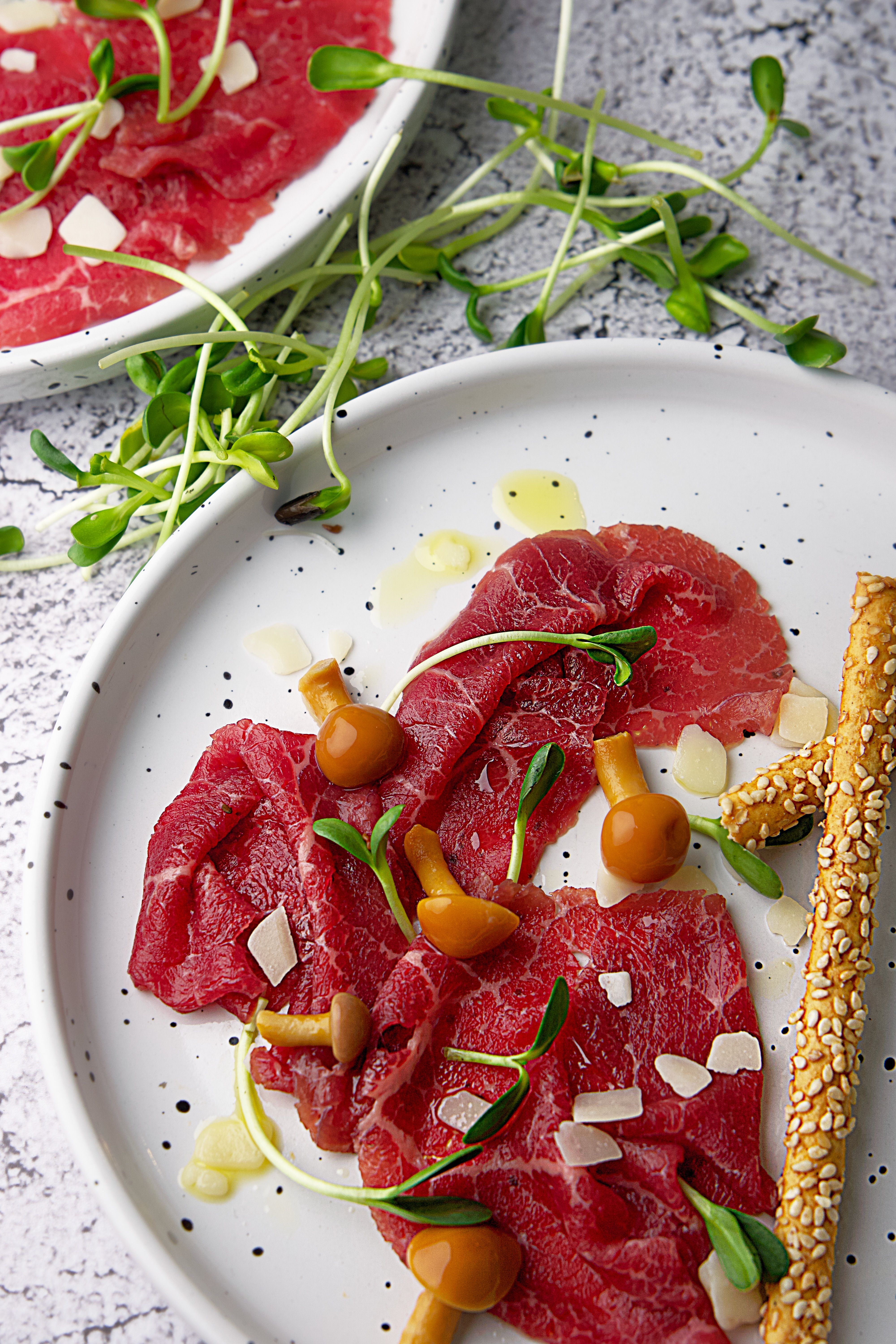 Deep red, thinly sliced bresaola fanned out on a white plate with a drizzle of olive oil, lemon wedges, and shaved parmesan on top