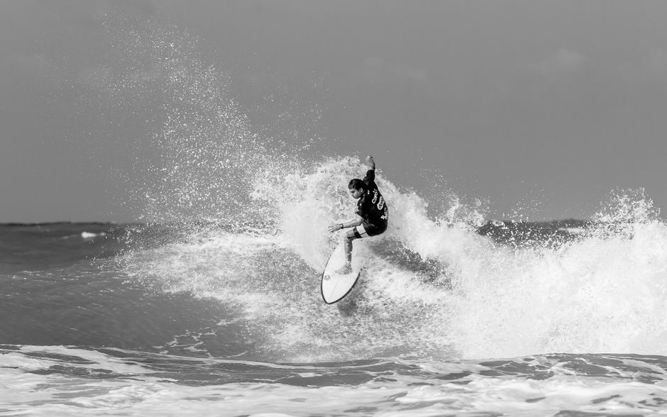 Black and white photo of a surfer catching a wave, capturing motion and energy.