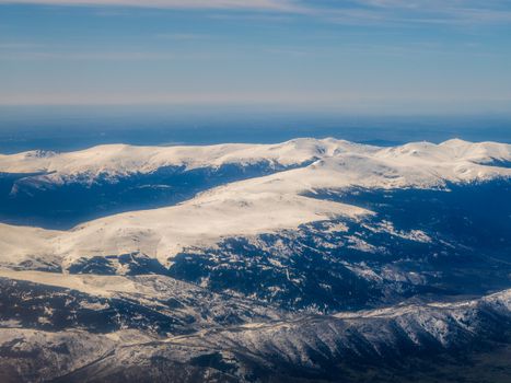Breathtaking aerial view showcasing a vast snow-covered mountain range against a serene sky.