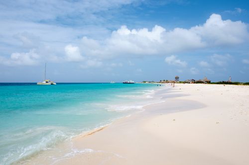 Free A serene Caribbean beach with turquoise water, white sand, and boats under a bright blue sky. Stock Photo