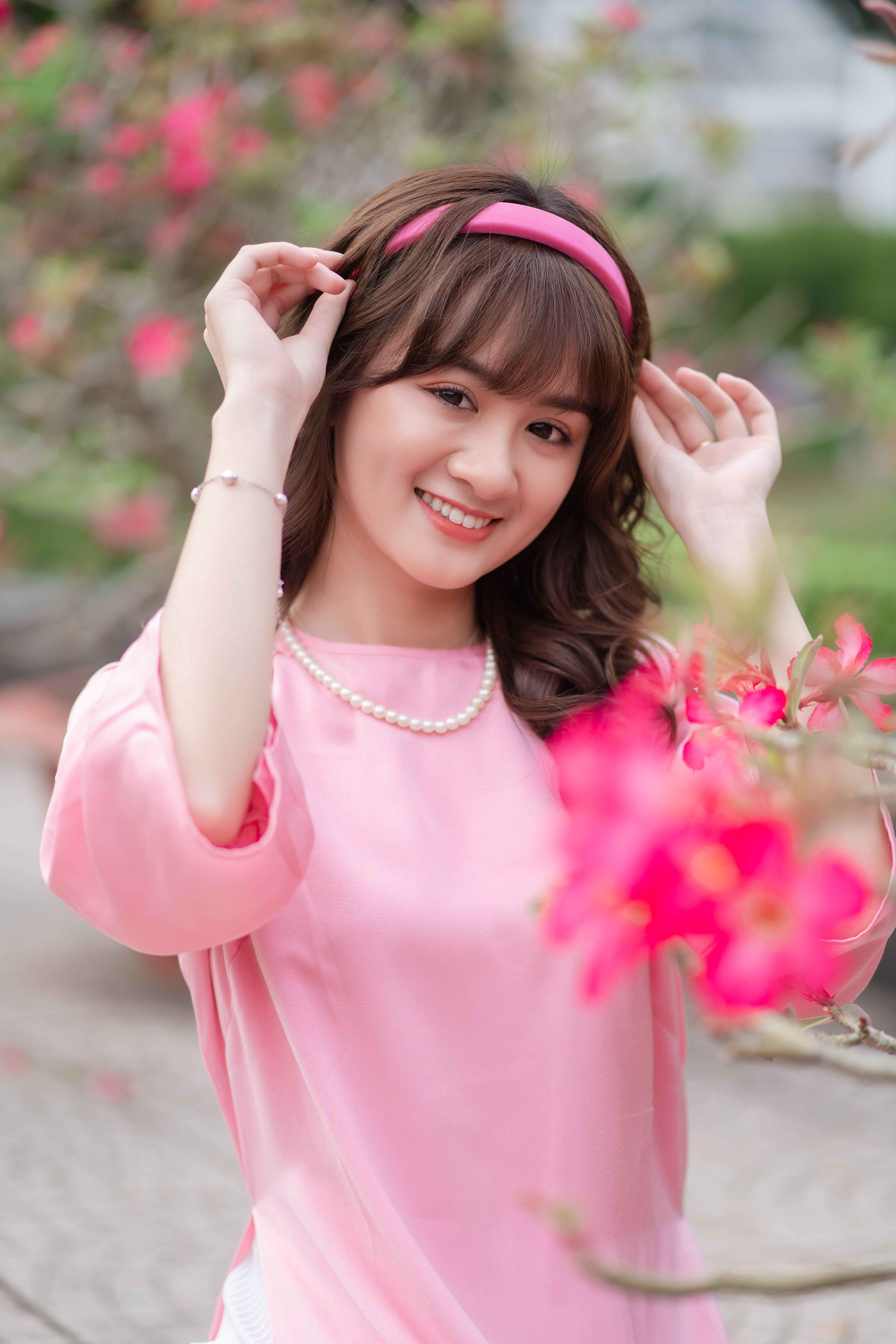 Portrait of a smiling woman in a pink dress surrounded by vibrant flowers outdoors.