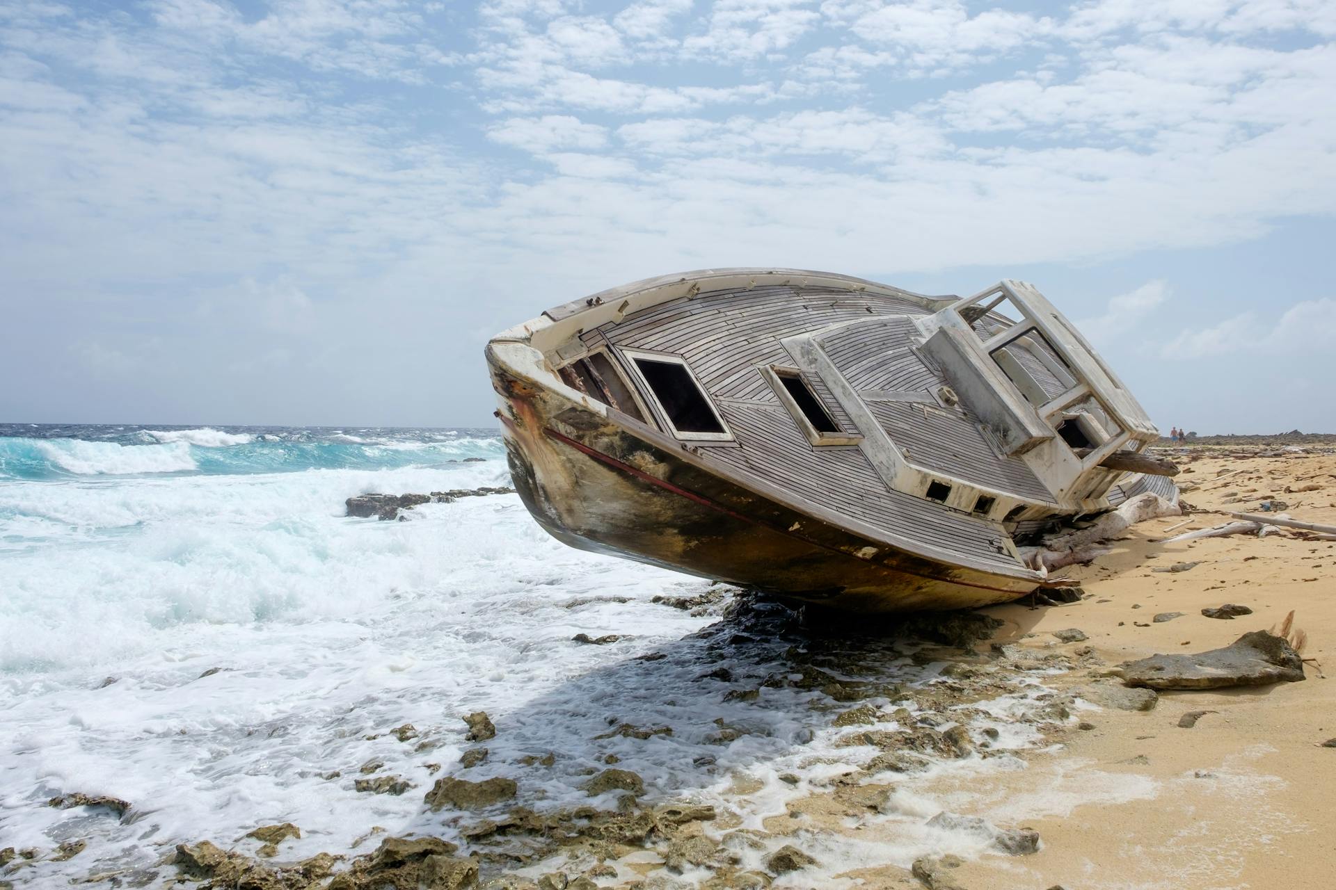 A captivating shipwreck lies on a sandy beach with crashing waves under a partly cloudy sky.