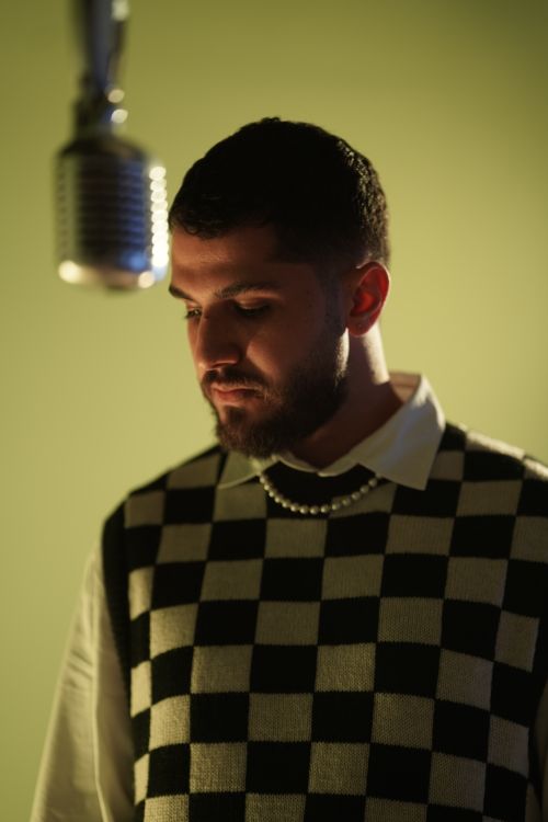 Free Musician in a checkered sweater under a microphone, indoor studio scene. Stock Photo