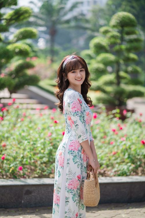 Free Woman in floral dress smiling in a vibrant park with flowerbed, perfect for summer vibes. Stock Photo