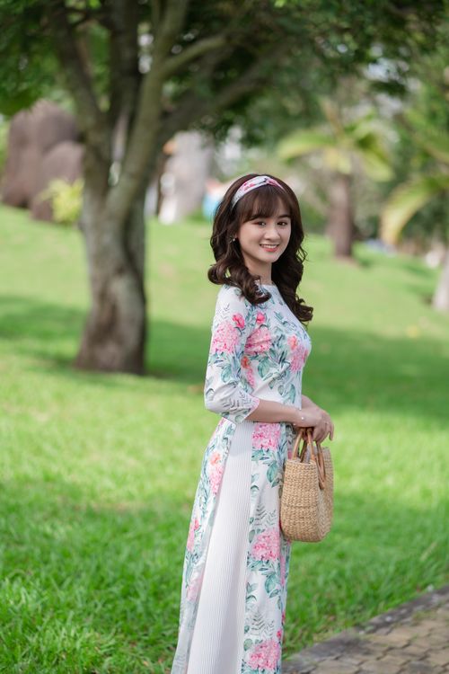 Free Smiling woman in a floral dress enjoying a sunny day outdoors, holding a wicker handbag. Stock Photo