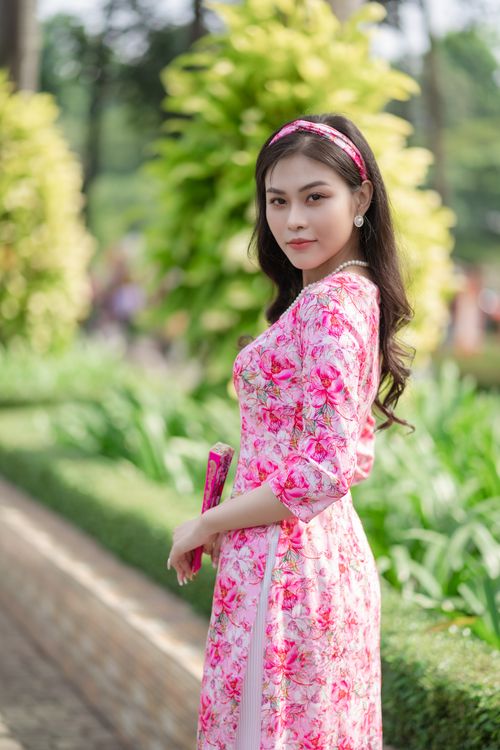 Free Elegant woman in a floral pink dress standing outdoors, surrounded by greenery. Stock Photo
