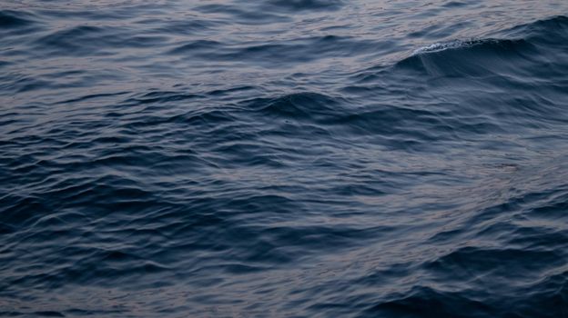 Gentle dark ocean waves creating a natural pattern at twilight, offering a calming and deep visual experience.
