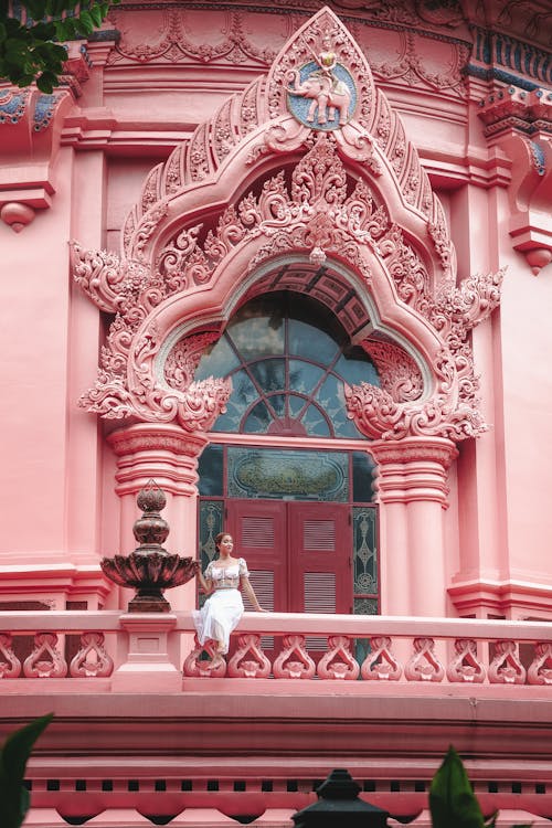 Woman Sitting on Balcony of Traditional Ornate Pink Mansion