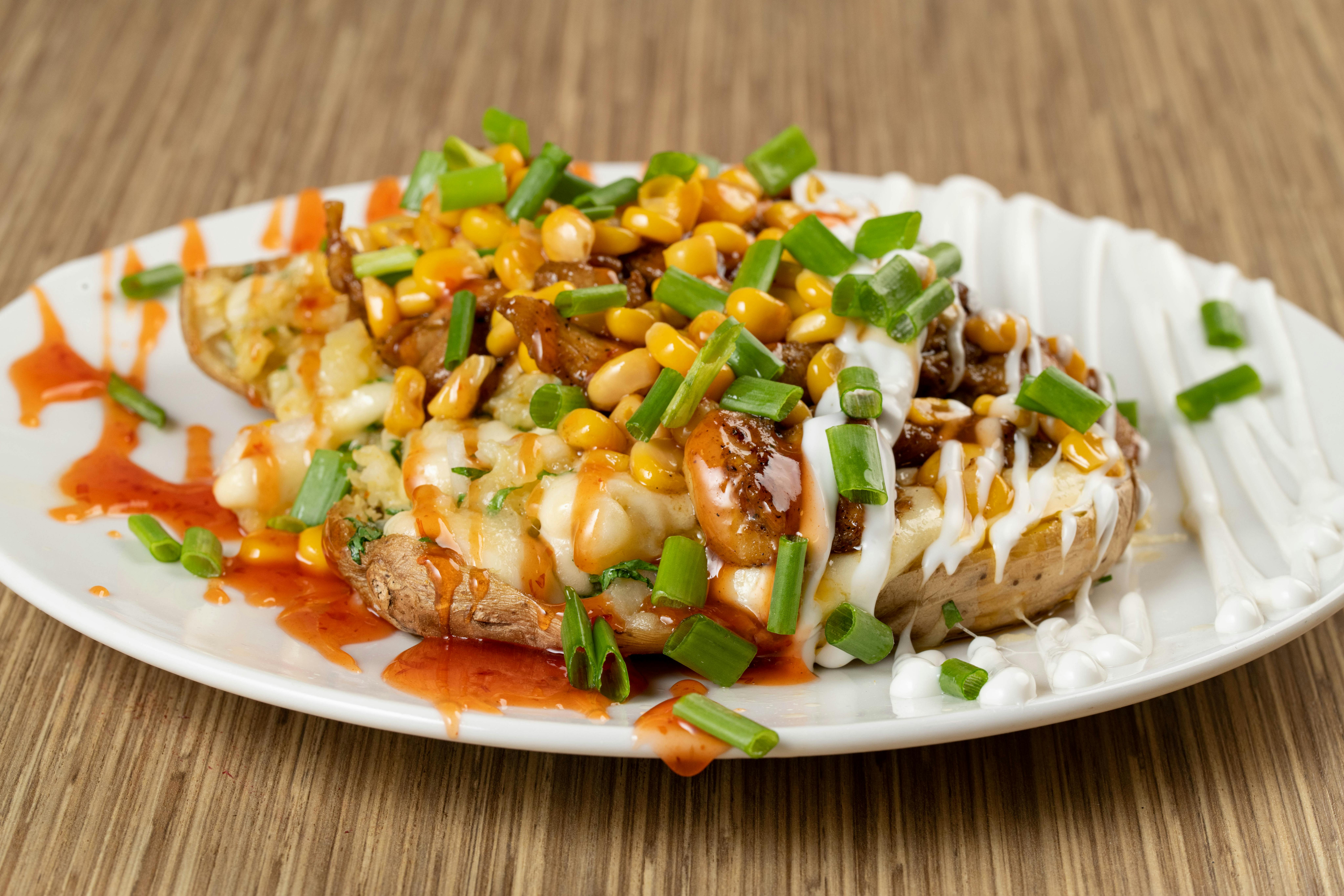 Delicious loaded baked potato with cheese, corn, and chives, drizzled with sauces.