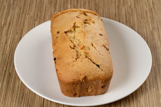 A close-up of a freshly baked fruit loaf on a white plate, resting on a wooden surface.