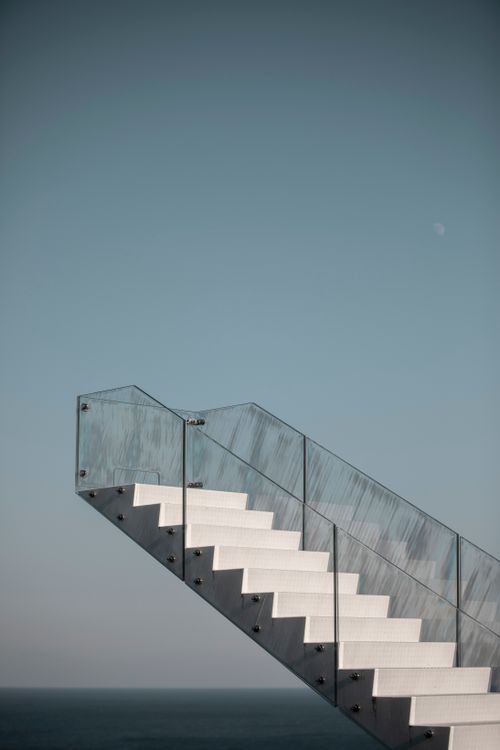 Free A modern staircase with glass railing leading skyward, set against an expansive blue sky. Stock Photo