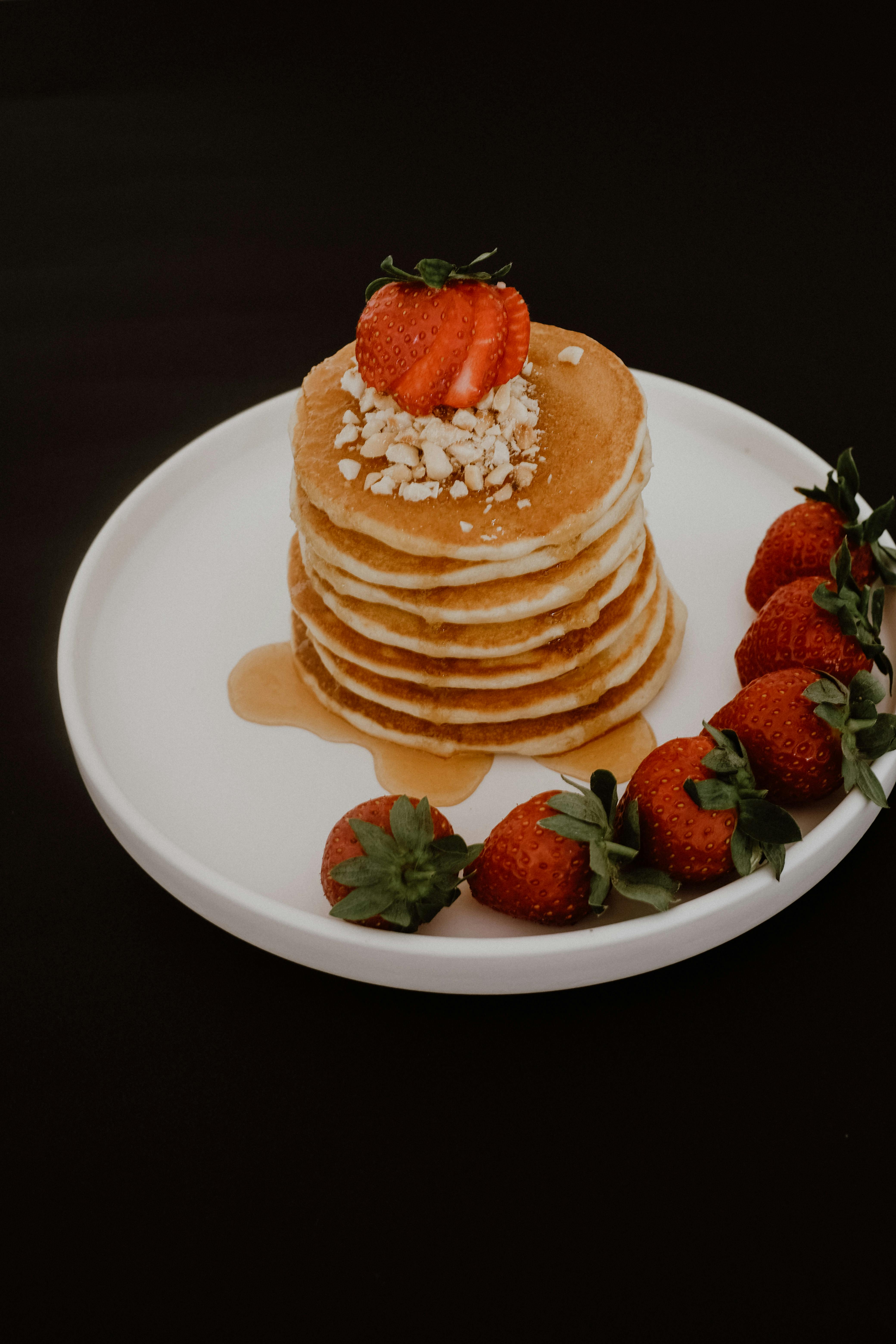Delicious stack of pancakes topped with strawberries and nuts, drizzled with maple syrup.