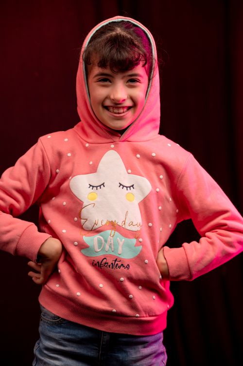 Free Young girl in a pink star hoodie smiling confidently with hands on waist. Studio portrait. Stock Photo