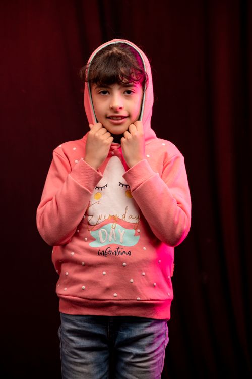 Free A cheerful child with curly hair in a pink hoodie posing indoors with a dark background. Stock Photo