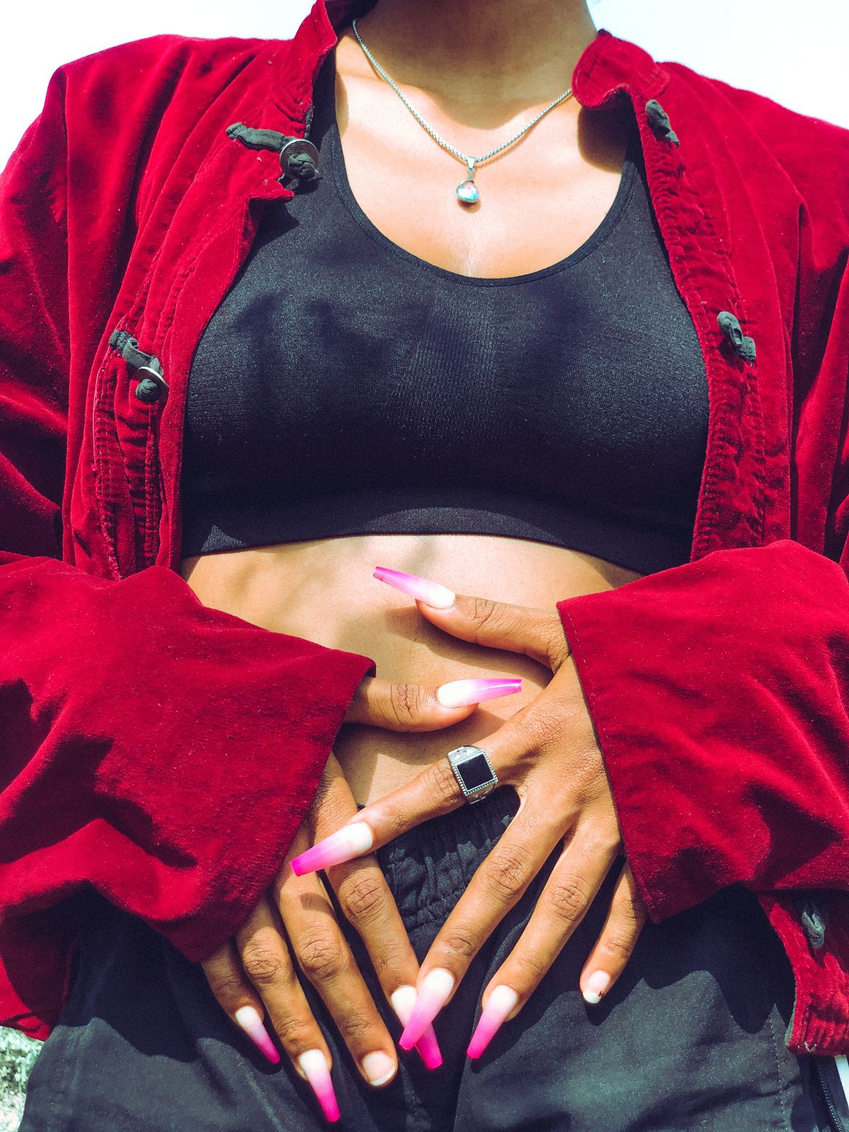 Fashionable woman in red velvet jacket with pink nails, shot from waist up outdoors.