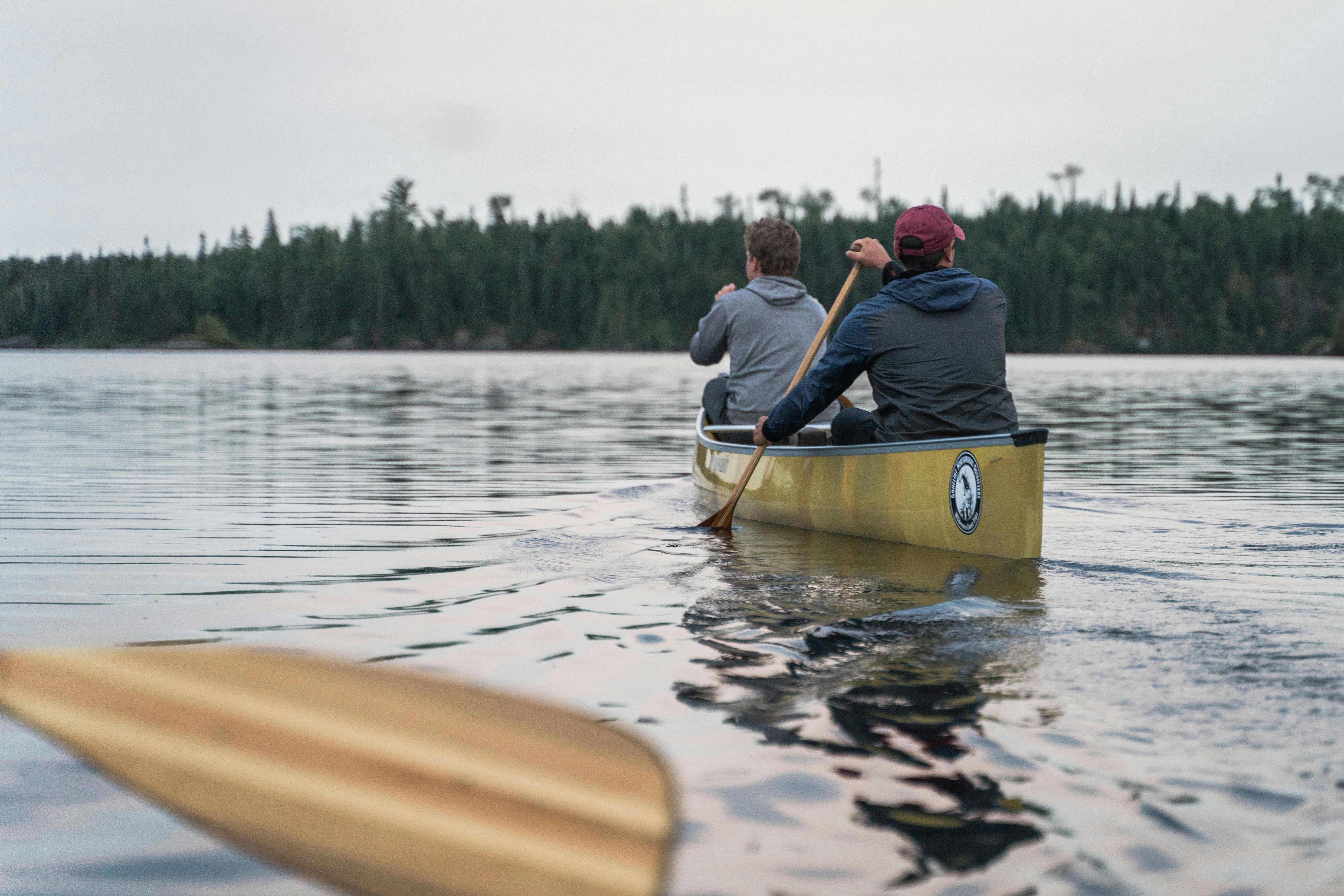 Two people canoeing on a serene lake surrounded by forest in Ely, Minnesota.
